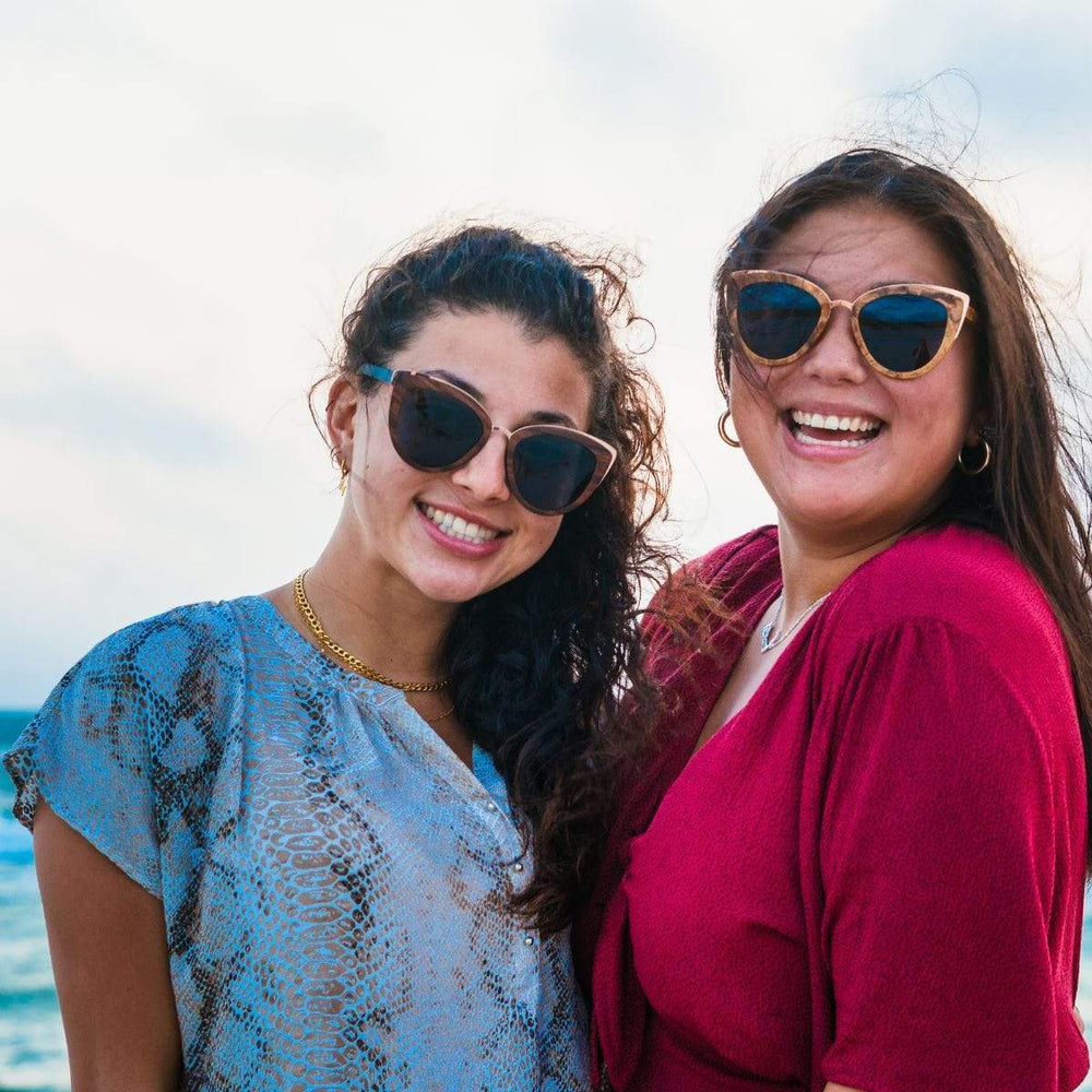 Two Models Wearing Wooden Bombshell Sunglasses With Smoke Lenses At The Beach